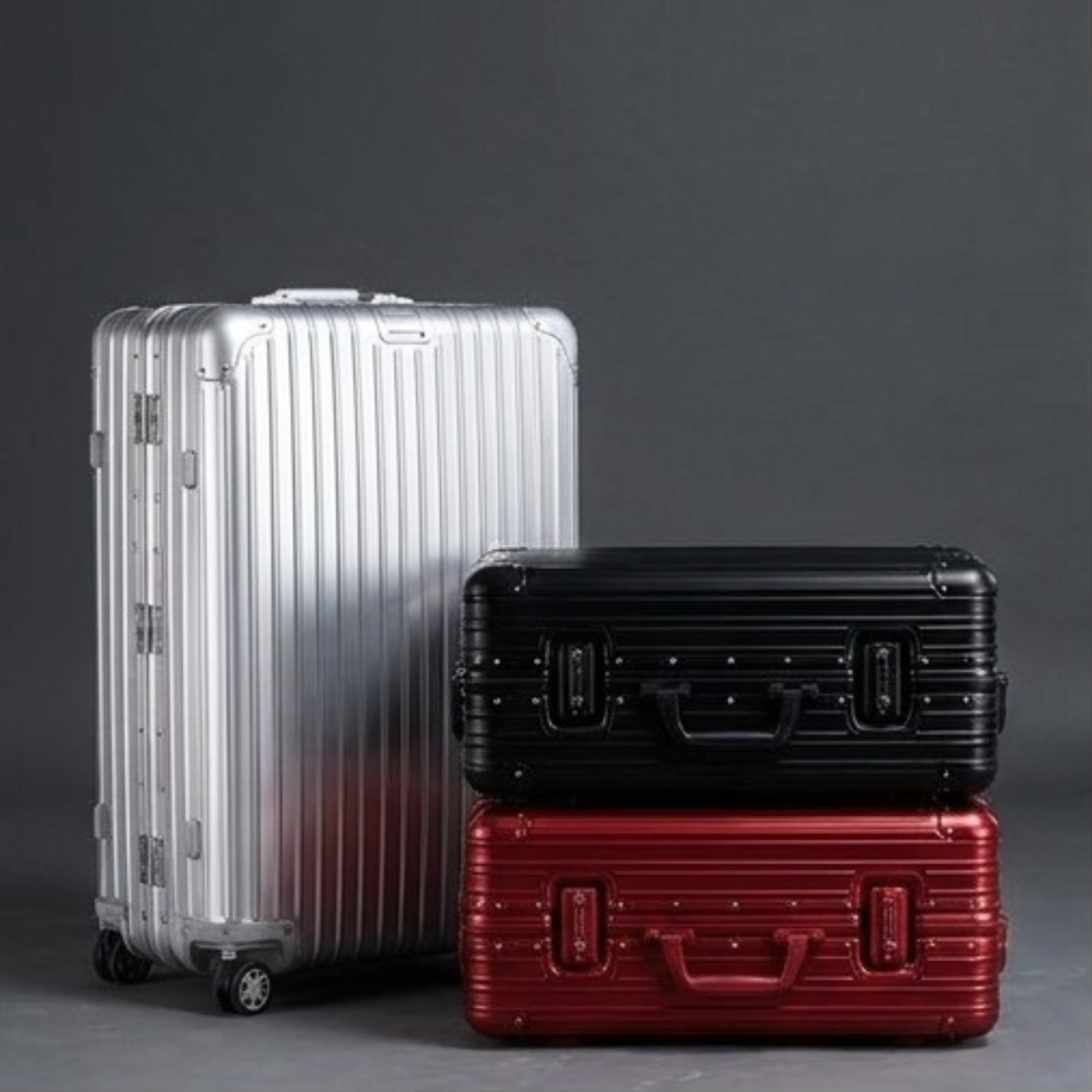 SPRITZ™ Bourdain Suitcase in silver, black, and red aluminum hard-shell finishes, upright and side by side